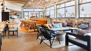 A spacious, well-lit cafe with large windows, wooden furniture, and a variety of seating options. - Holiday Home in Nieuwvliet-Bad near Beach (Nieuwvliet)