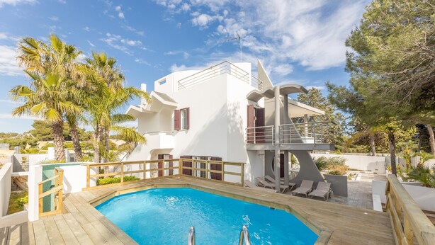 Une villa moderne dotée d’une piscine, d’une terrasse en bois et d’une façade blanche.
