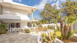 Une maison moderne à deux étages dotée d’un patio agrémenté d’un jardin de cactus et de mobilier d’extérieur.