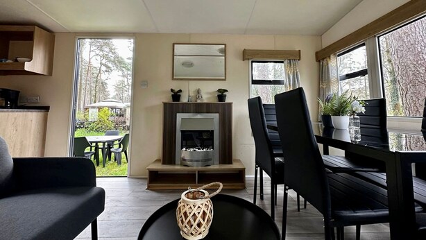 Un salón moderno con chimenea, muebles negros y ventanas amplias que ofrecen vistas al exterior.