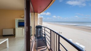 Un balcon avec vue sur la plage, une télévision et une chaise.