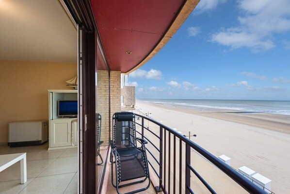 A balcony with a view of the beach, a TV, and a chair.