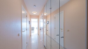 Un couloir aux murs blancs, doté d’un sol carrelé et de portes à panneaux de verre.