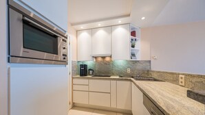 Une cuisine moderne avec des armoires blanches, un four à micro-ondes encastré et un plan de travail en granit.