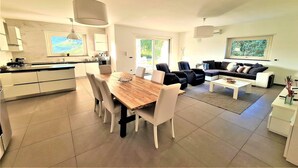 A modern kitchen with white cabinets, a wooden dining table, and a black sofa in the living area.