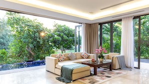 Ein modernes Wohnzimmer mit einem beigefarbenen Sofa, einem Couchtisch und Blick auf üppiges Grün draußen.