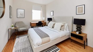 Ein modernes Schlafzimmer mit einem großen Bett, einem Schreibtisch, einem Stuhl, einem Nachttisch mit Lampe sowie Kunstwerken an den Wänden.