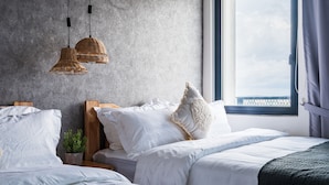 Une chambre moderne avec un mur en béton, une grande fenêtre offrant une belle vue et deux lampes suspendues en osier.