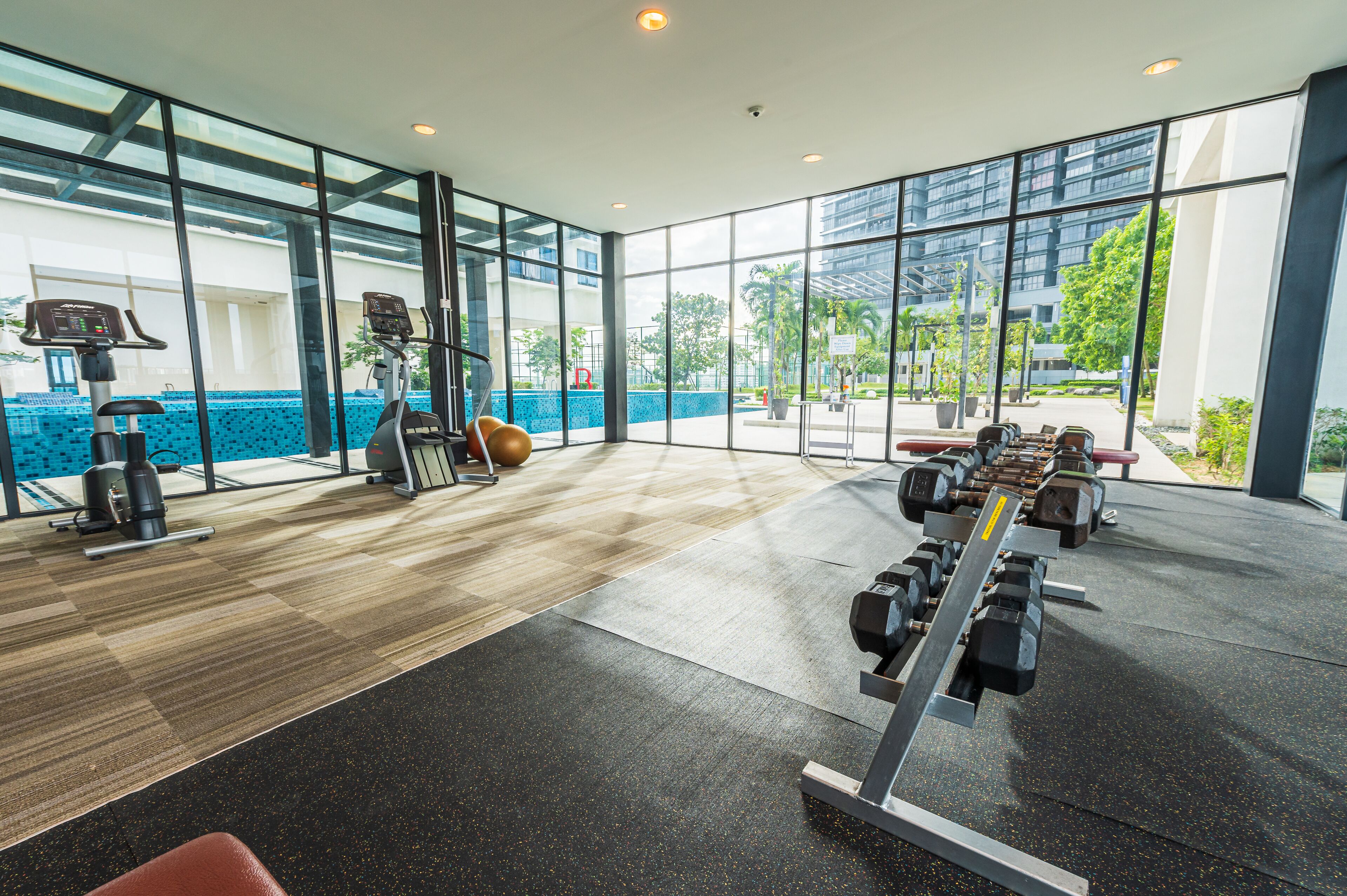 Une salle de sport moderne équipée d’appareils de cardio, de postes d’entraînement en musculation et de grandes fenêtres offrant une vue sur l’extérieur.