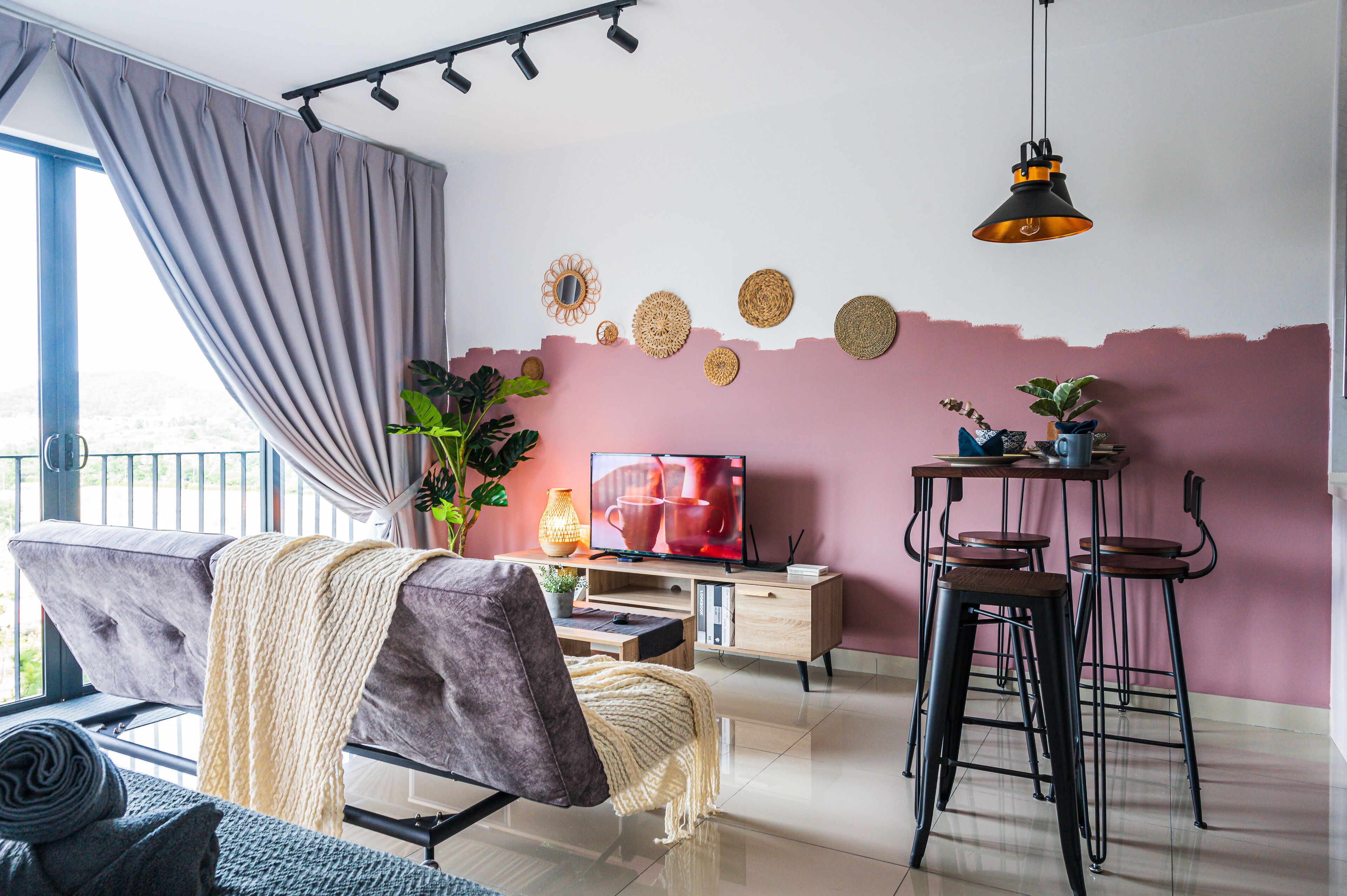 Un salon moderne comprenant un canapé, un téléviseur, une table basse et un coin repas avec des tabourets.