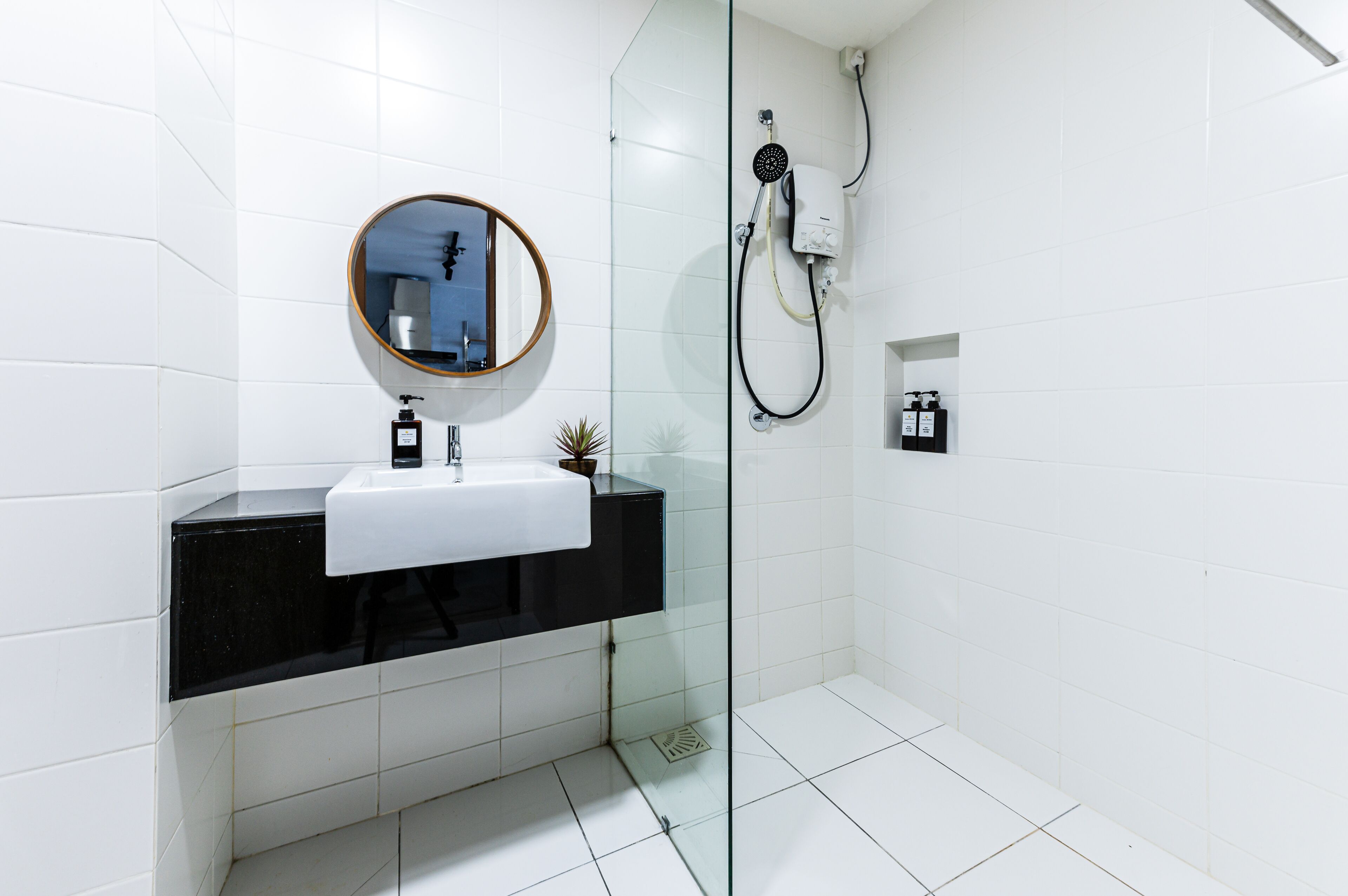 A modern bathroom with a black countertop sink, a round mirror, and a glass shower enclosure.