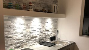 A compact kitchen with a stone backsplash, a stainless steel sink, and wooden cabinets. - MARMARAKI Village  (Kos)