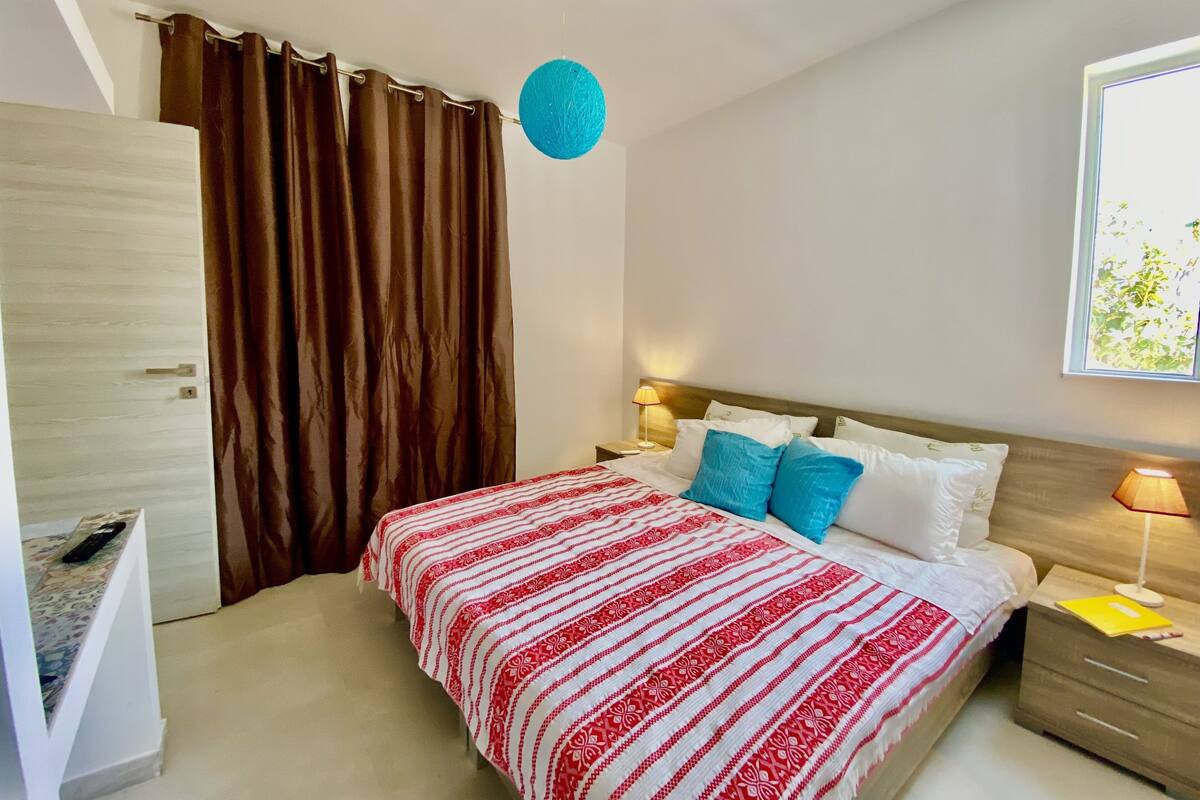 A bedroom with a bed, curtains, a lamp, and a window.