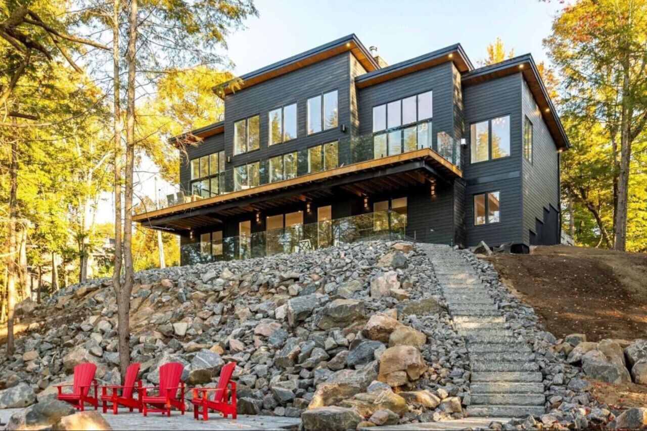 Une maison moderne à deux étages, dotée d’un escalier en pierre menant à une terrasse en bois.