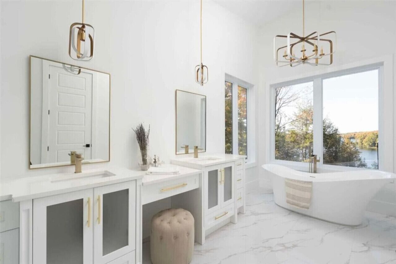 A modern bathroom with two sinks, a large bathtub, and a window with a view of trees.