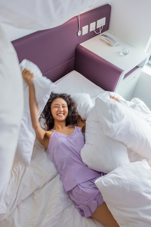 A bed with white bedding and a purple headboard.