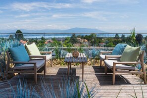 A wooden deck with two lounge chairs and a table, overlooking a scenic view of a body of water and distant mountains. - YOTEL Geneva Lake (Founex)