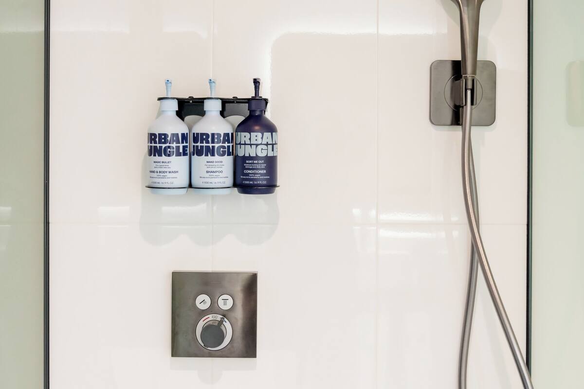 A modern bathroom with a glass shower enclosure, a handheld showerhead, and three bottles of Urban Jungle products.