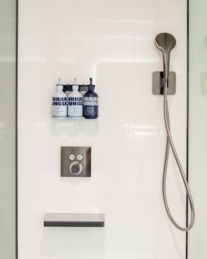 A modern bathroom with a glass shower enclosure, a handheld showerhead, and three bottles of Urban Jungle products.