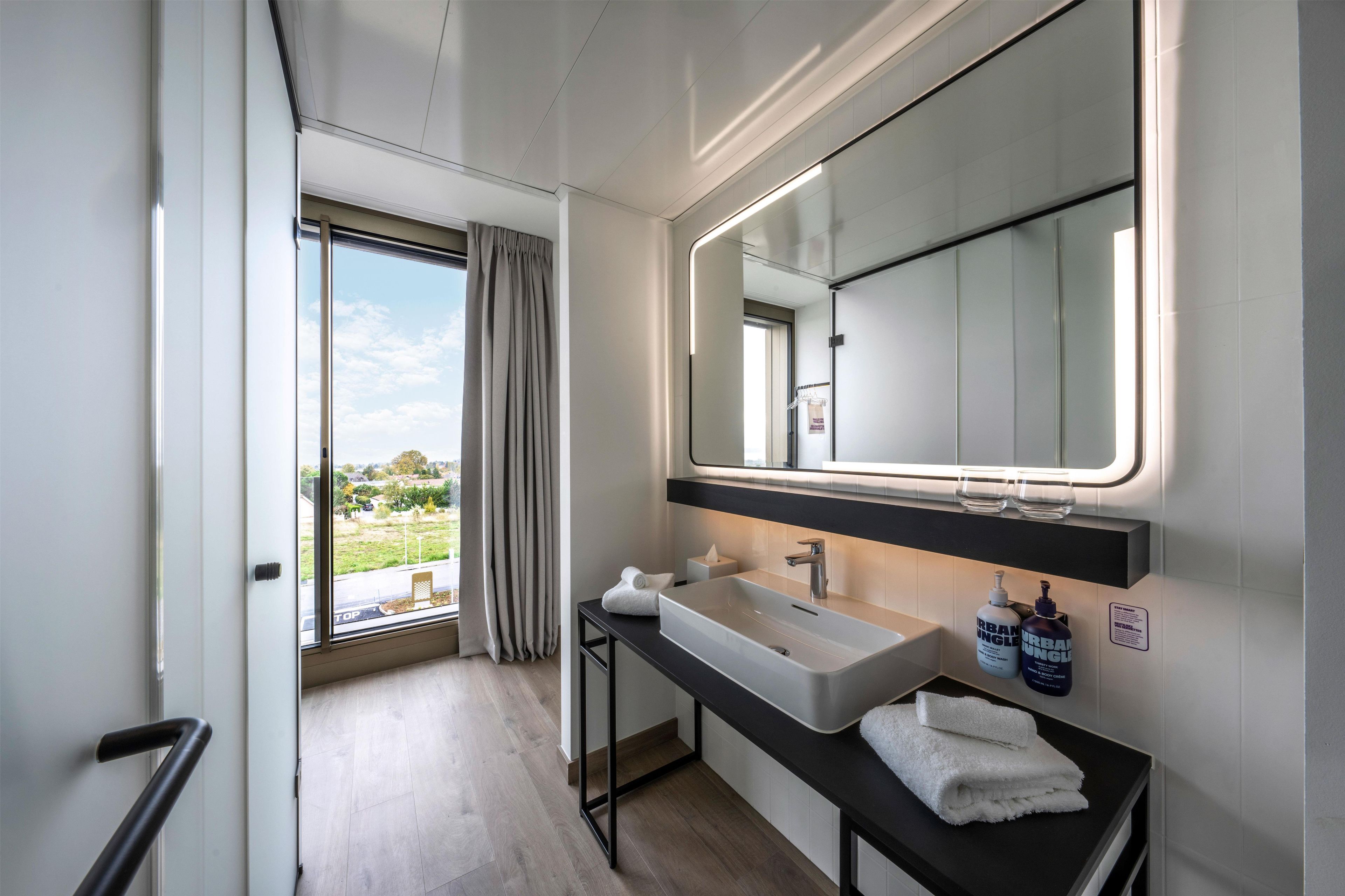 A modern bathroom with a large window, a sink, a mirror, and a towel rack.