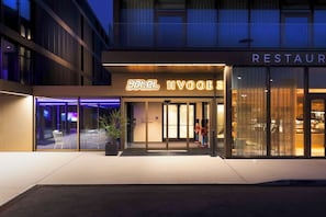 A hotel with a restaurant on the ground floor, featuring a modern facade, glass doors, and outdoor seating. - YOTEL Geneva Lake (Founex)