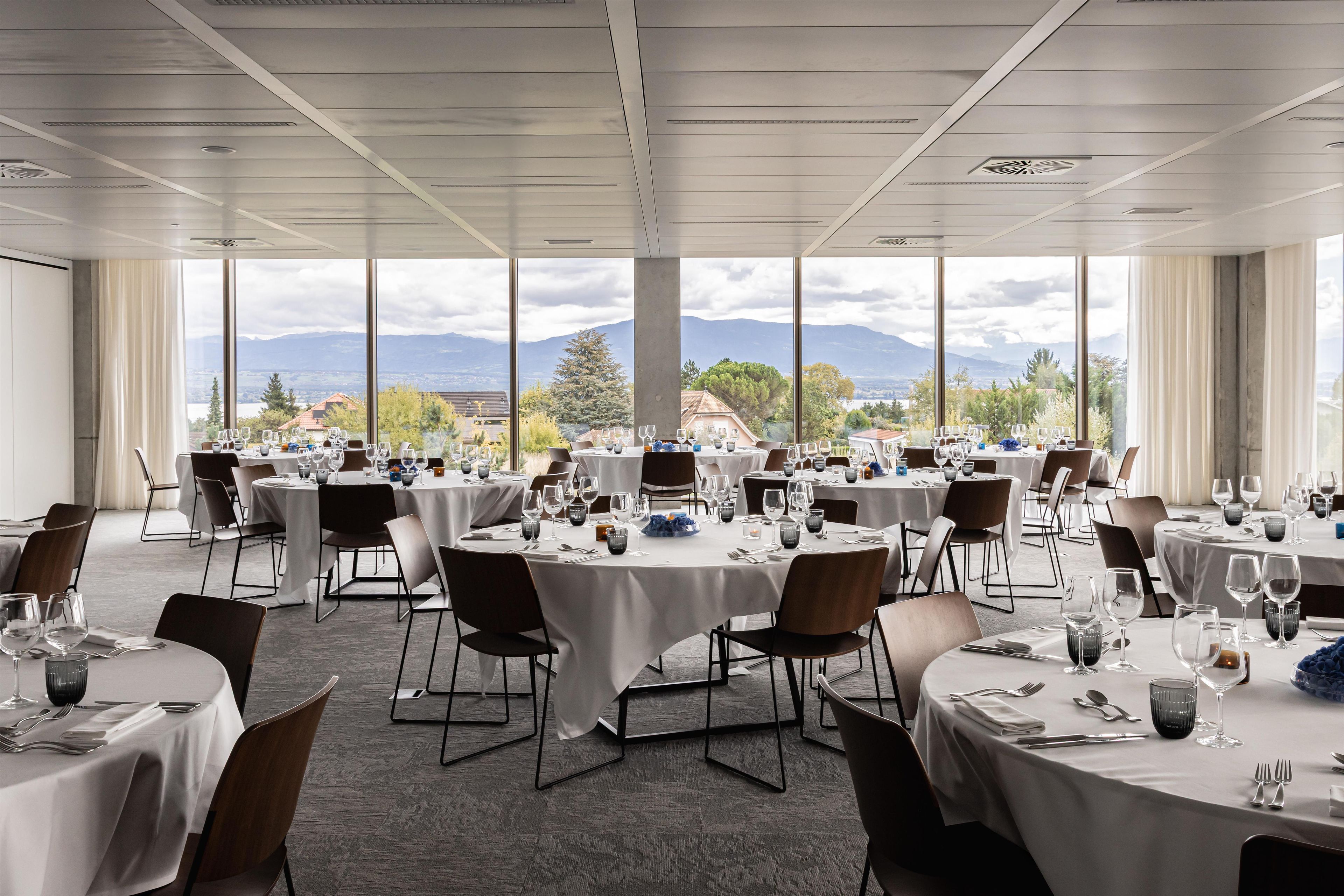A spacious dining area with multiple round tables, each set with white tablecloths and chairs.