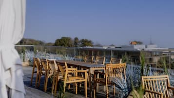 Une terrasse sur le toit, dotée de tables et de chaises en bois, et agrémentée de plantes en pot.