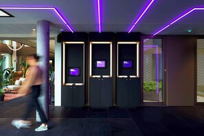 A modern lobby with a central column, three dark cabinets with screens, and purple LED lighting. - YOTEL Geneva Lake (Founex)