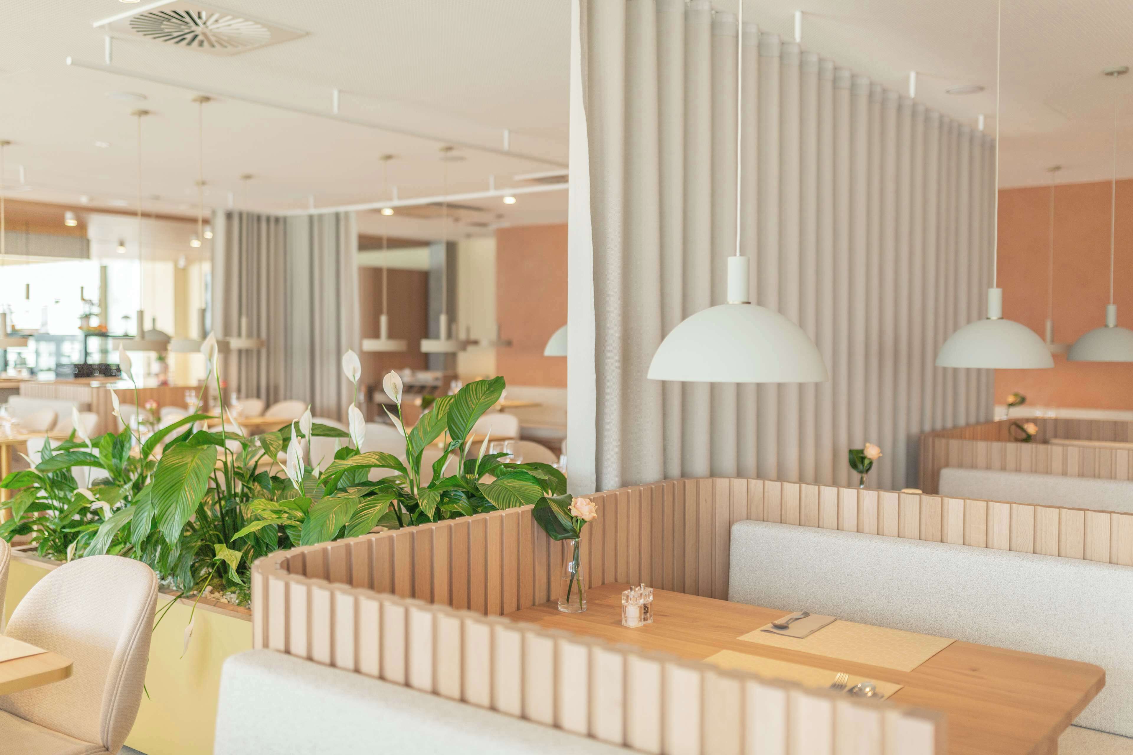 Un intérieur de restaurant moderne avec des banquettes, des luminaires suspendus et des plantes en pot.