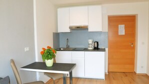 Una cocina compacta con armarios blancos, un lavamanos de acero inoxidable, una cafetera y una puerta de madera.