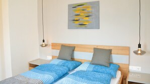 Una cama doble con cabecera de madera, dos mesitas de noche, un cuadro abstracto gris y dos lámparas colgantes.