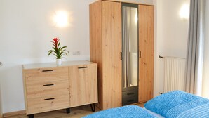 Un dormitorio con un armario de madera, una cama con ropa de cama azul y una planta en maceta sobre el tocador.