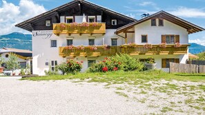 A two-story building with balconies, a gravel driveway, and a mountainous backdrop.