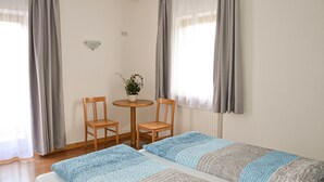 Ein Zimmer mit einem Bett, zwei Stühlen, einem kleinen Tisch mit Pflanze und einem Fenster mit Vorhängen.