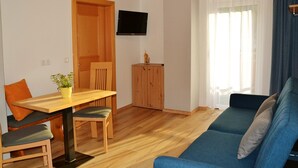 Una sala de estar con una mesa de comedor de madera, sillas, un sofá azul, un mueble de madera y un televisor en la pared.
