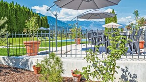 Un espacio al aire libre rodeado por una cerca, con plantas en macetas, una piscina y sillas.