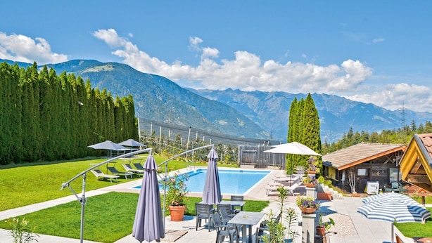 Un espace piscine doté de chaises longues et de parasols, entouré de montagnes et de verdure.