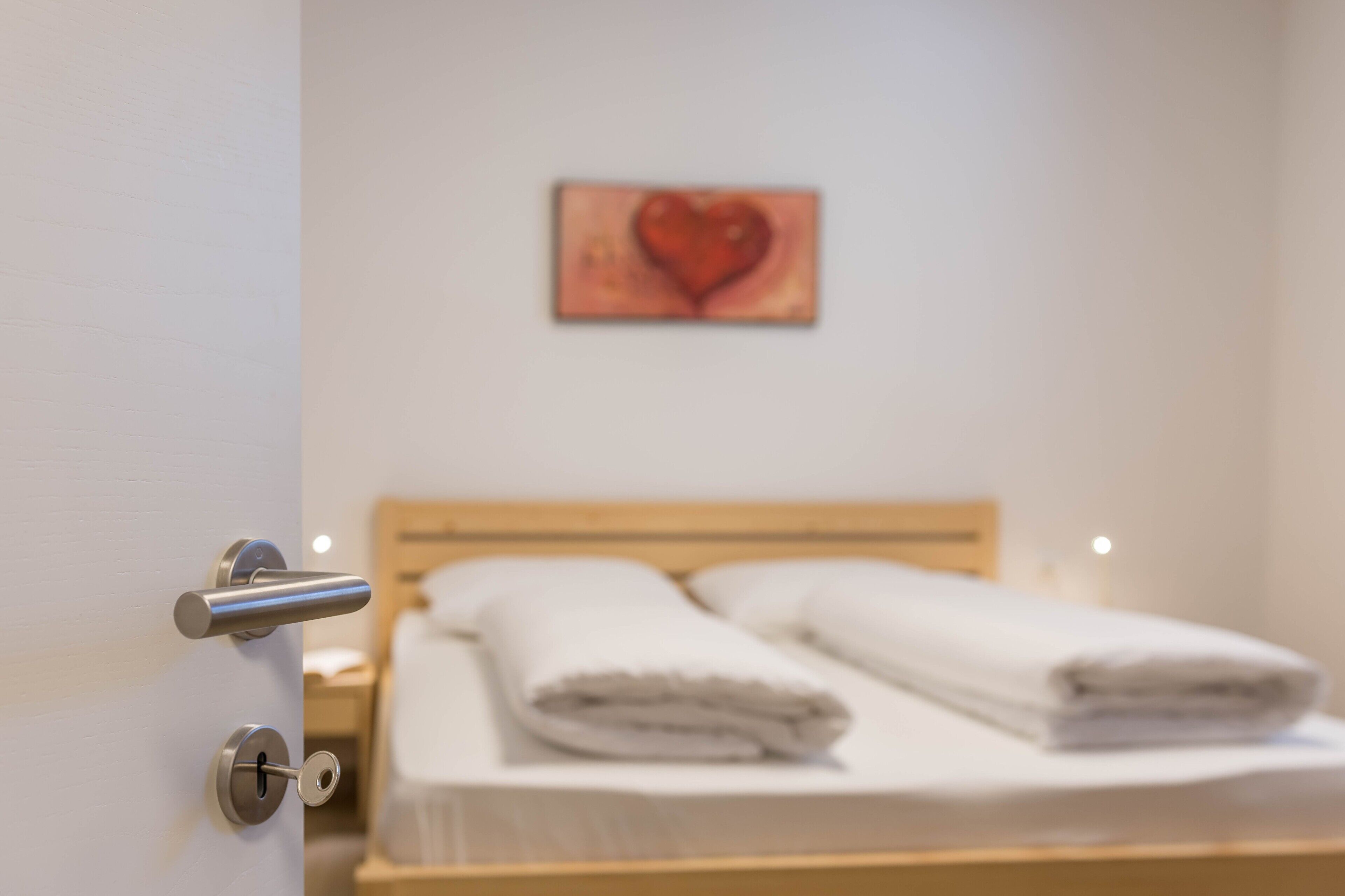 Habitación de hotel con cama, una puerta con mirilla y una obra de arte con forma de corazón en la pared.