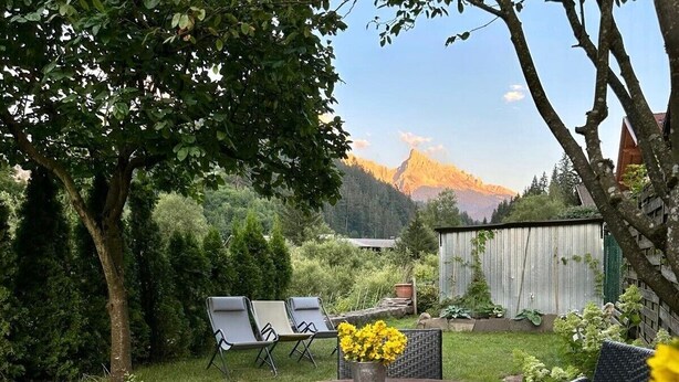 Een terras met een ronde tafel, twee stoelen en een bloevas.