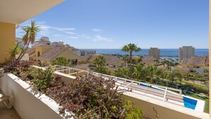 Ein Balkon mit Pool, Palmen und Blick auf Meer und Gebäude.