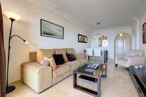 A living room with a sofa, a coffee table, a floor lamp, and a dining area with chairs and a table.