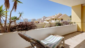 Ein Balkon mit Liegestuhl, Palmen und Blick auf das Meer und die Bebauung.