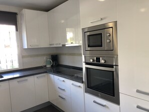 Una cocina con gabinetes blancos, horno de acero inoxidable y microondas.
