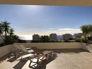 A terrace with two lounge chairs, a view of the sea, and buildings in the background. - Holiday Apartment 'Amazing In Puerto Alto' with Sea View, Shared Pool & Wi-Fi (Estepona)