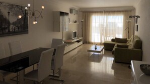 A modern living room with a dining area, a sofa, a TV, and a painting on the wall. - Holiday Apartment 'Amazing In Puerto Alto' with Sea View, Shared Pool & Wi-Fi (Estepona)