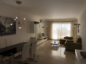 Una sala moderna con comedor, sofá, televisión y un cuadro en la pared.