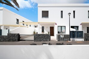 Un immeuble résidentiel moderne à deux étages, doté d’un toit plat, d’un porche couvert et d’une entrée sécurisée par un portail.