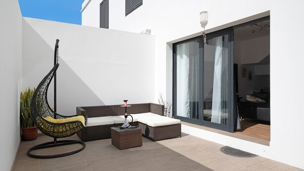 A modern outdoor seating area with a swing chair, a cushioned bench, and a small table. - Vacation Home "Gardenia" with Mountain View, Private Terrace & Wi-Fi (Costa Teguise)