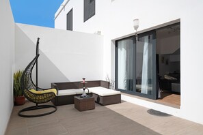 A modern outdoor seating area with a swing chair, a cushioned bench, and a small table. - Vacation Home "Gardenia" with Mountain View, Private Terrace & Wi-Fi (Costa Teguise)