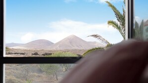 A window view of a desert landscape with mountains and sparse vegetation. - Vacation Home "Gardenia" with Mountain View, Private Terrace & Wi-Fi (Costa Teguise)